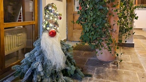 A Christmas tree with a Santa Claus figure, a potted plant with ivy, and a stone-tiled floor.