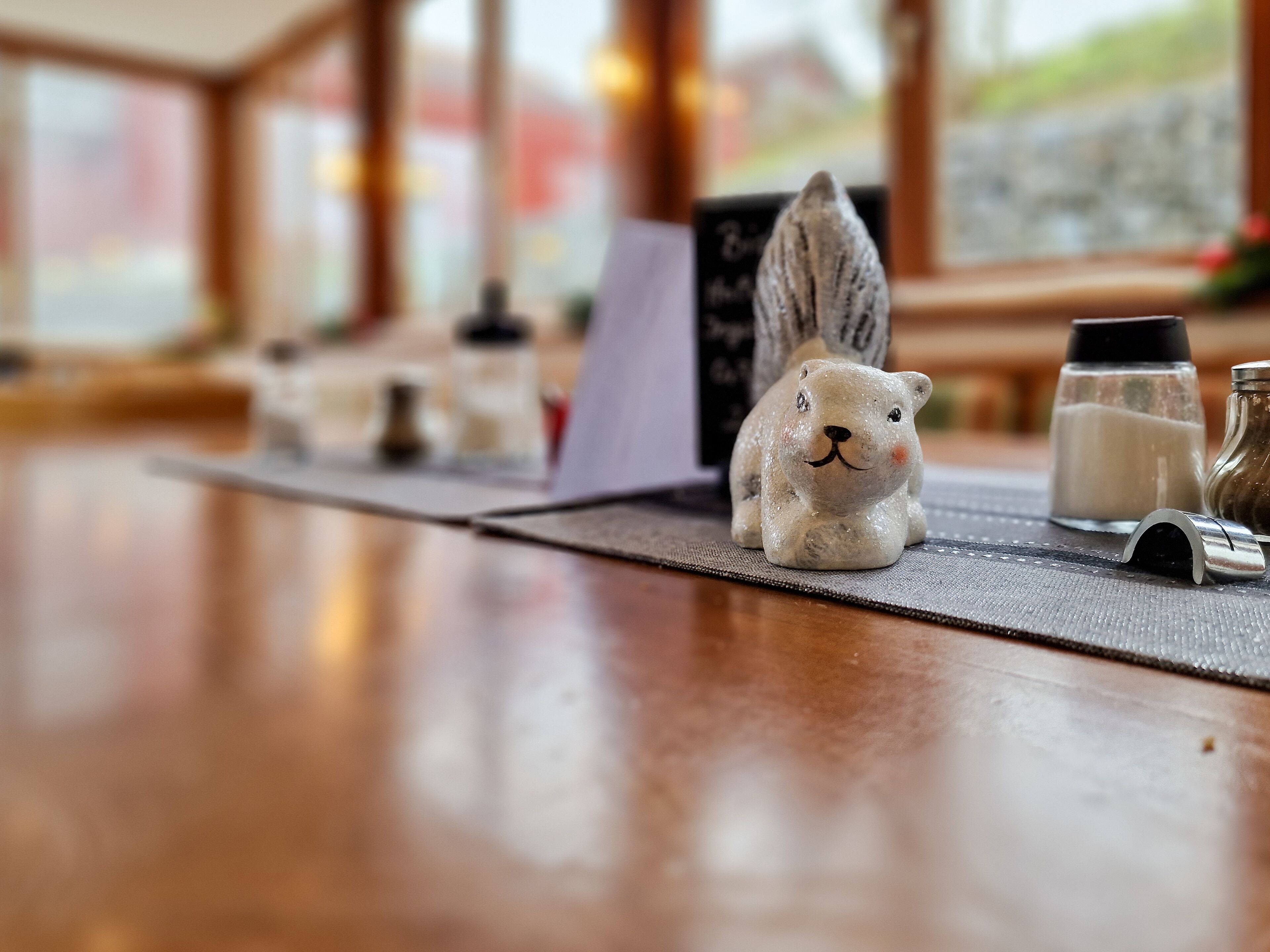 A wooden table with a ceramic rabbit figurine, salt and pepper shakers, and a menu board in a restaurant setting.