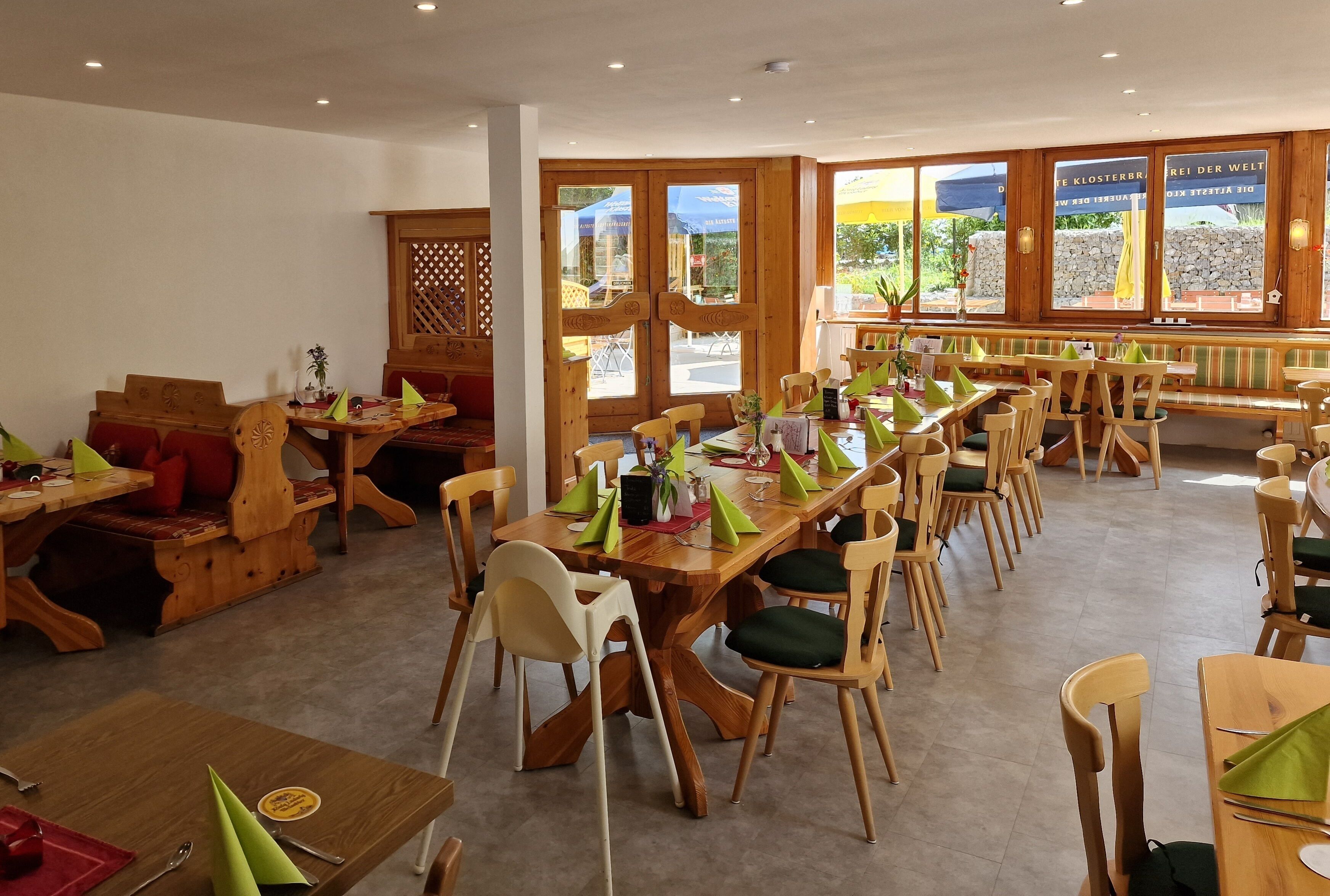 A restaurant with wooden furniture, green napkins, and large windows with outdoor views.