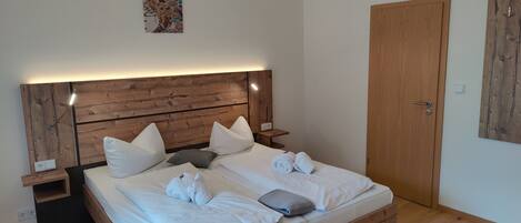A neatly made bed with white linens and pillows, a wooden headboard, a bedside table with a lamp, and a door to the right.