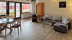 A modern living room with a glass coffee table, a sofa with striped cushions, wooden chairs, a wooden cabinet, and a view of the outside balcony.