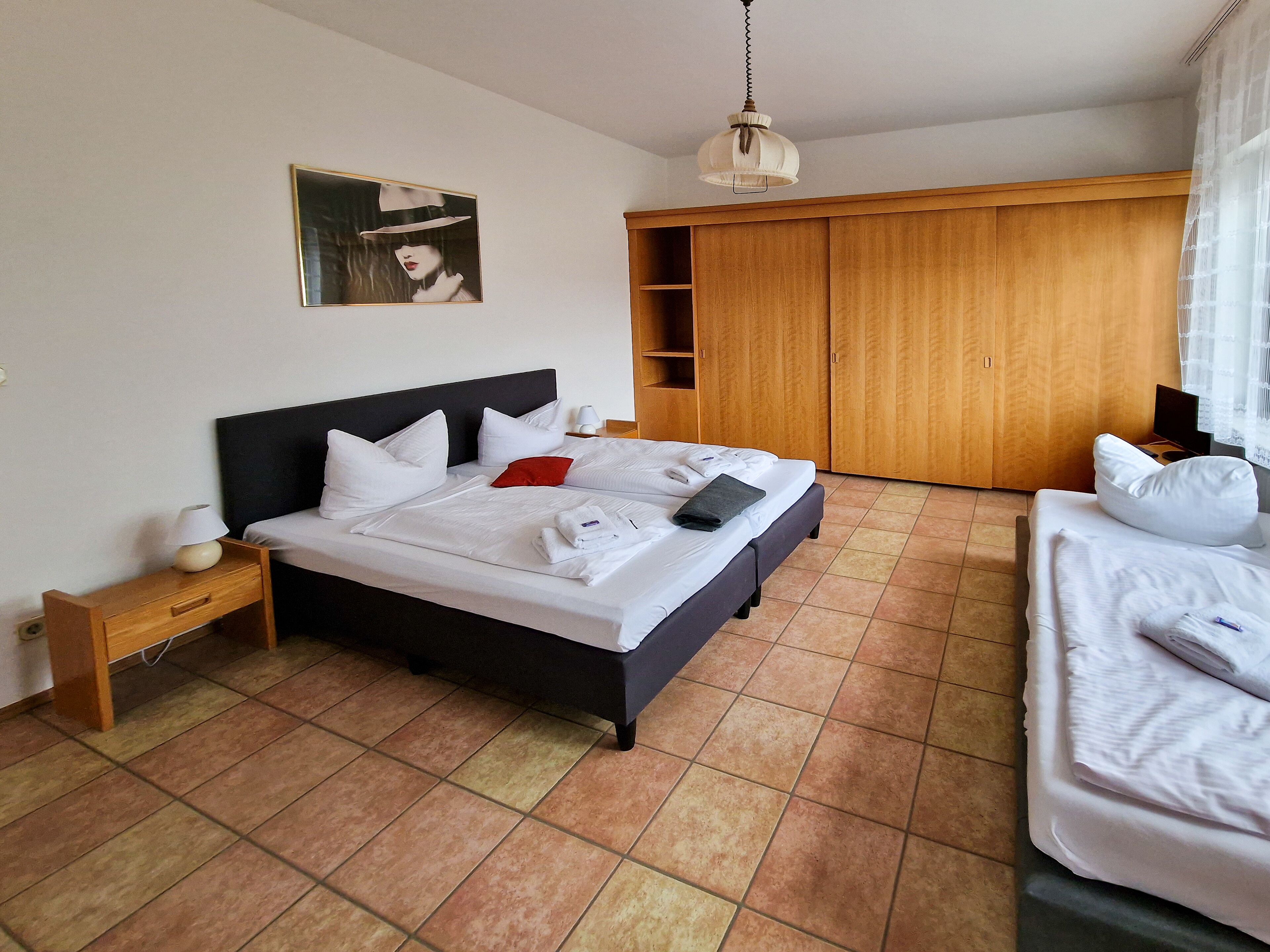 A neatly made bed with white linens, a bedside table with a lamp, and a wooden wardrobe.