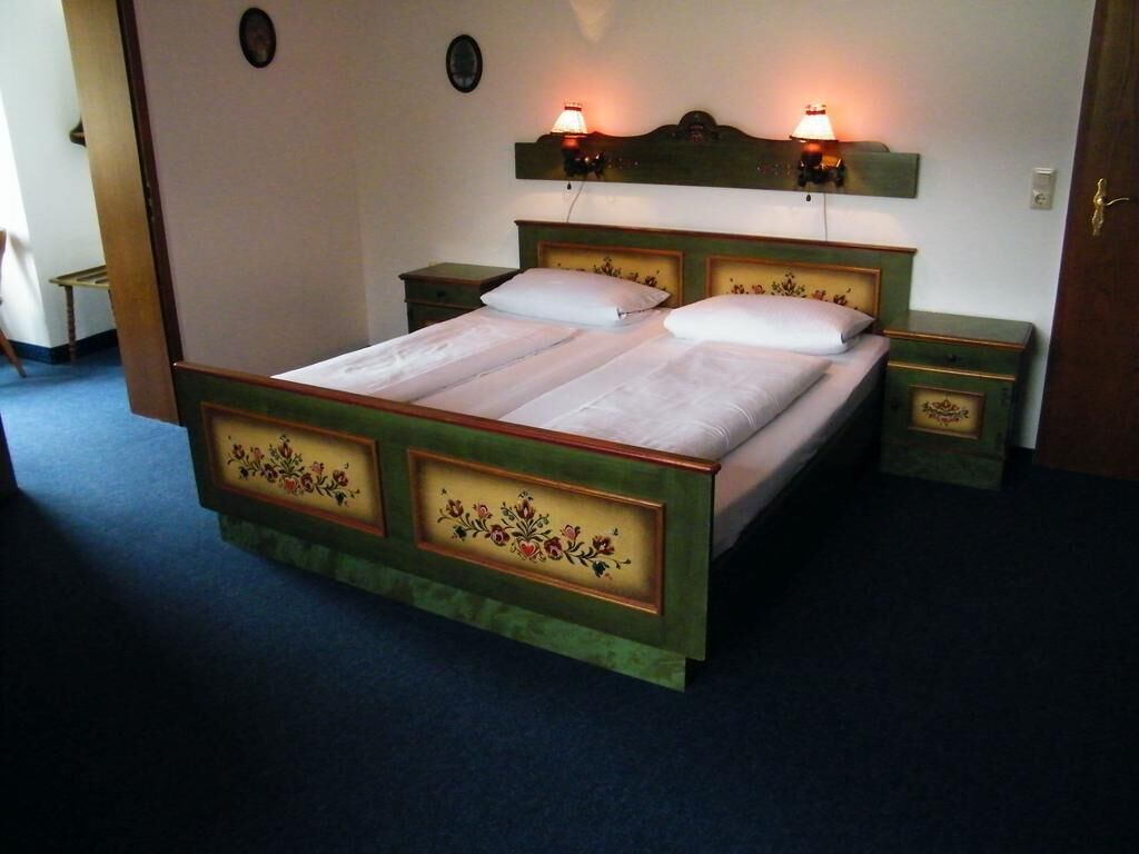 A double bed with floral headboard and footboard, bedside tables, and wall-mounted lamps.