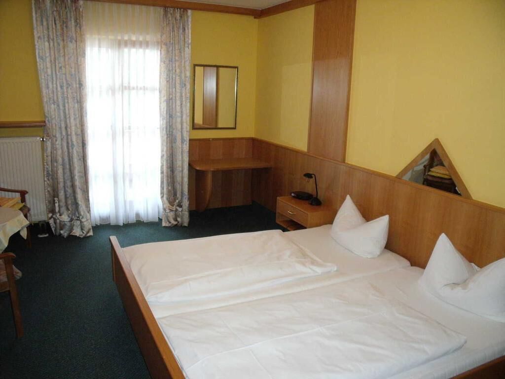Ein Hotelzimmer mit einem großen Bett, einem Holz-Kopfteil, einem Nachttisch, einem Spiegel und einem Fenster mit Vorhängen.