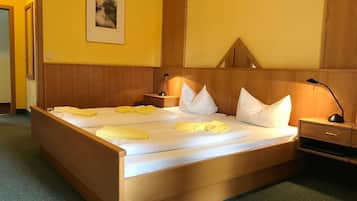 Una cama bien hecha con ropa de cama blanca y amarilla, un cabecero de madera, una mesita de noche con una lámpara y un cuadro en la pared.