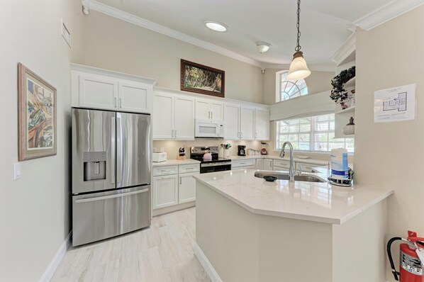 A modern kitchen with white cabinetry, stainless steel appliances, and a large island with a sink.