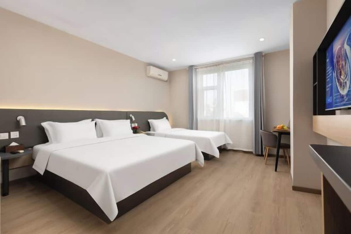 A hotel room with two beds, a TV, a desk, and a dining area.