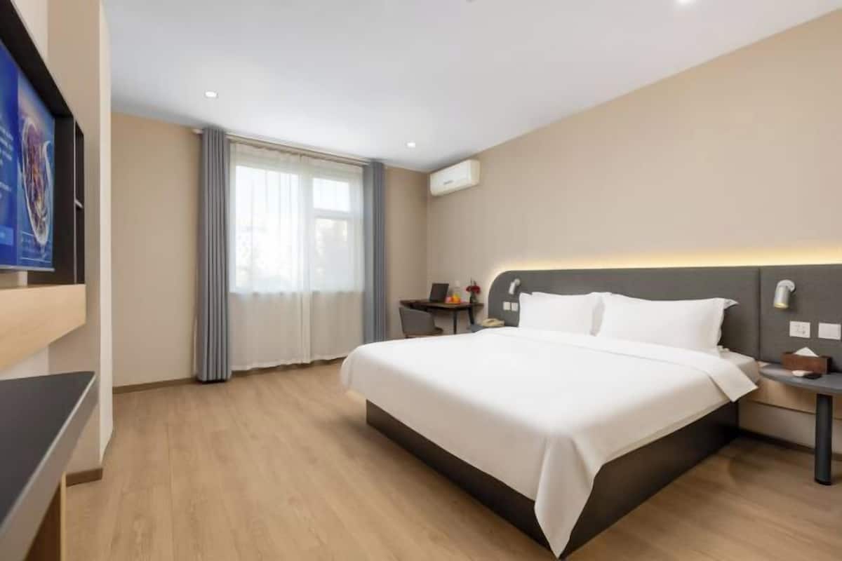 A hotel room with a large bed, a bedside table, a TV, and a window with curtains.