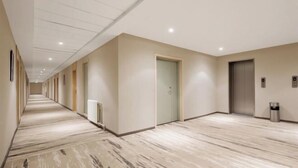A long, narrow hallway with a marble floor and beige walls, featuring doors and a trash can. - Jinjiang Inn (Weihai High-speed Railway North Station Oulefang Commercial Street Hotel) (Weihai)