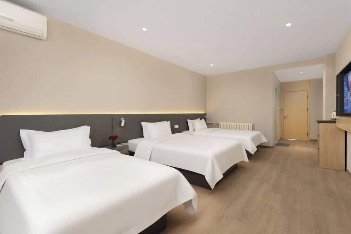 A hotel room with three single beds, a wooden floor, a white wall, and a television on the right side.