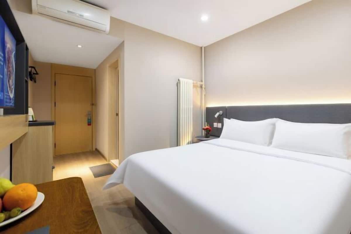 A hotel room with a bed, bedside table, and a wall-mounted TV.