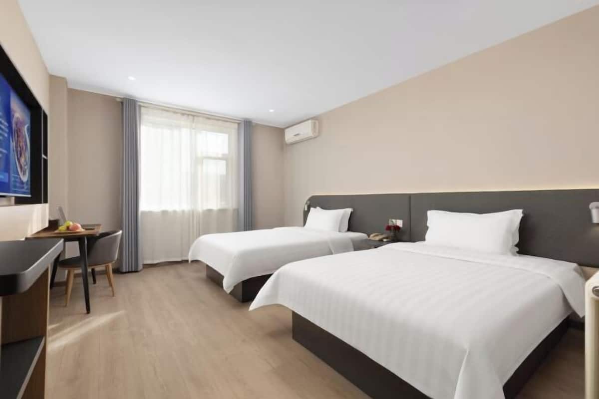A hotel room with two beds, a desk, a TV, and a window with curtains.