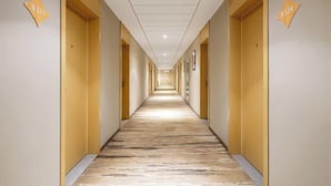 A hotel hallway with a marble floor, wooden doors, and numbered room signs. - Jinjiang Inn (Weihai High-speed Railway North Station Oulefang Commercial Street Hotel) (Weihai)