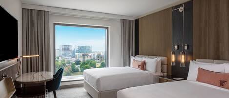 Une chambre d’hôtel avec deux lits, un bureau, une chaise, une télévision et une grande fenêtre donnant sur la ville.