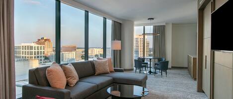 A modern hotel room with a large window, a sofa, a small table, and a TV.
