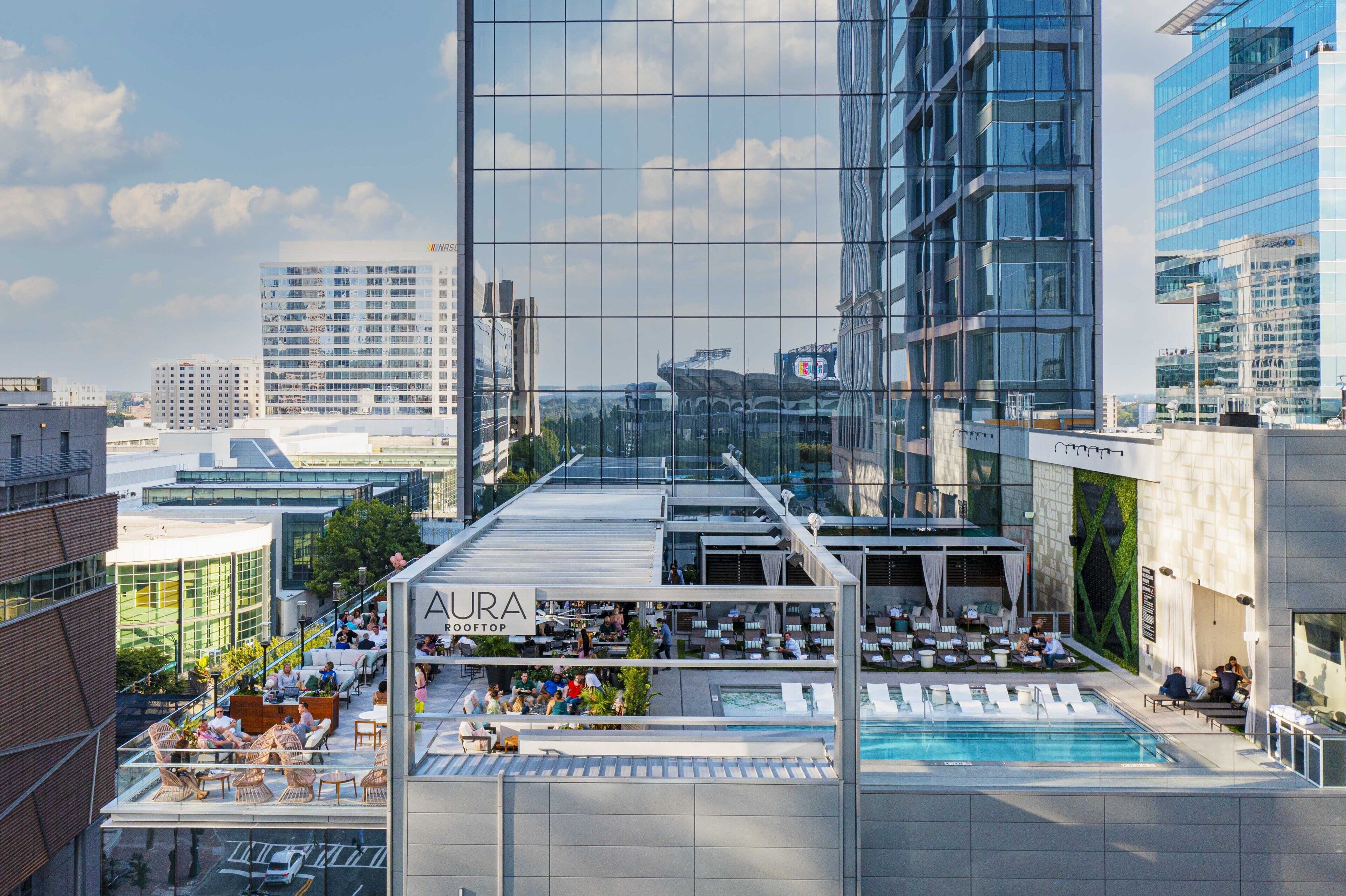A rooftop lounge area with outdoor seating and a pool, surrounded by modern buildings.