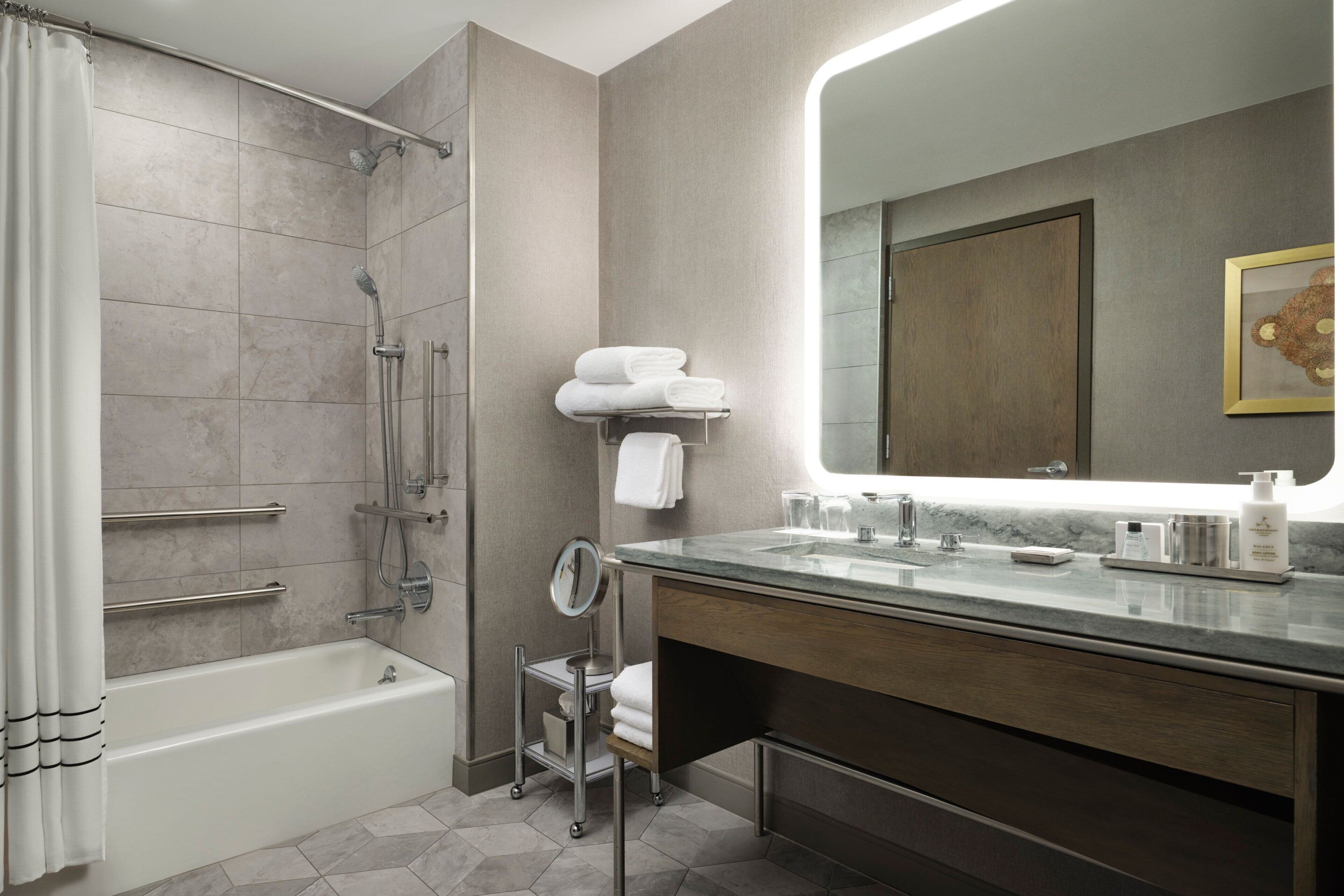 A modern bathroom with a bathtub, shower, vanity with a mirror, and neatly folded towels.