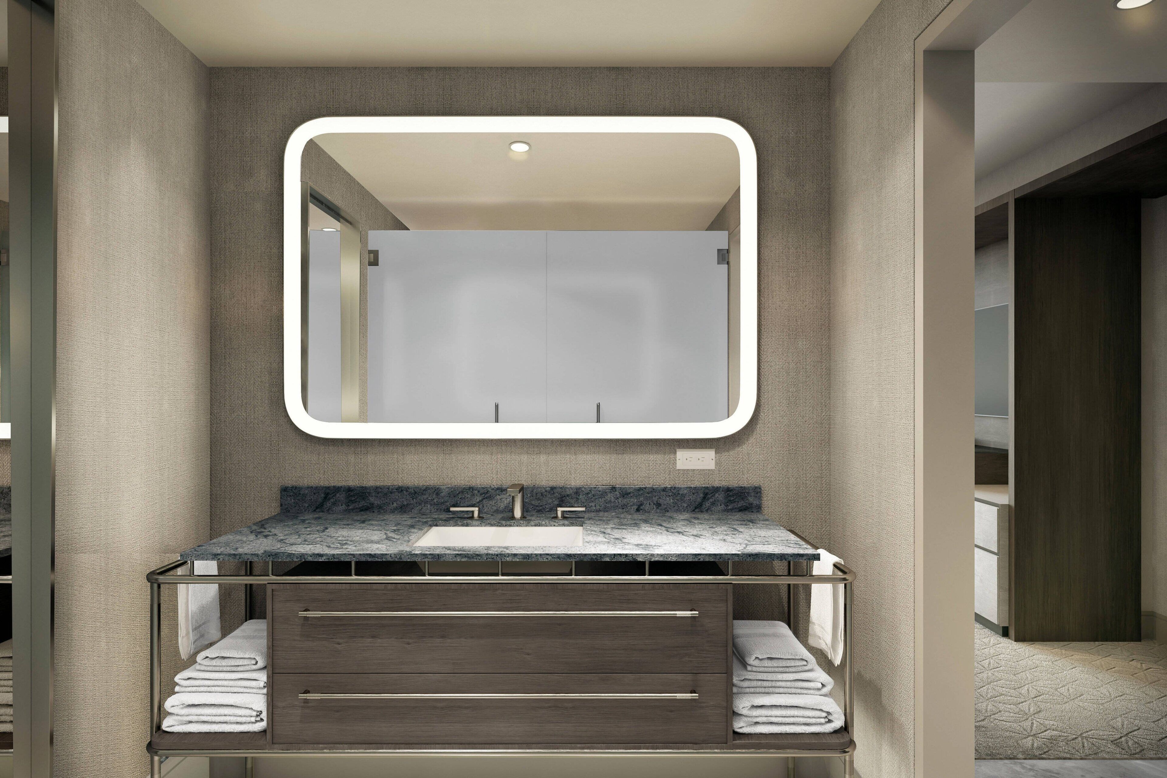 A modern bathroom with a marble sink, a large mirror, and neatly folded towels.