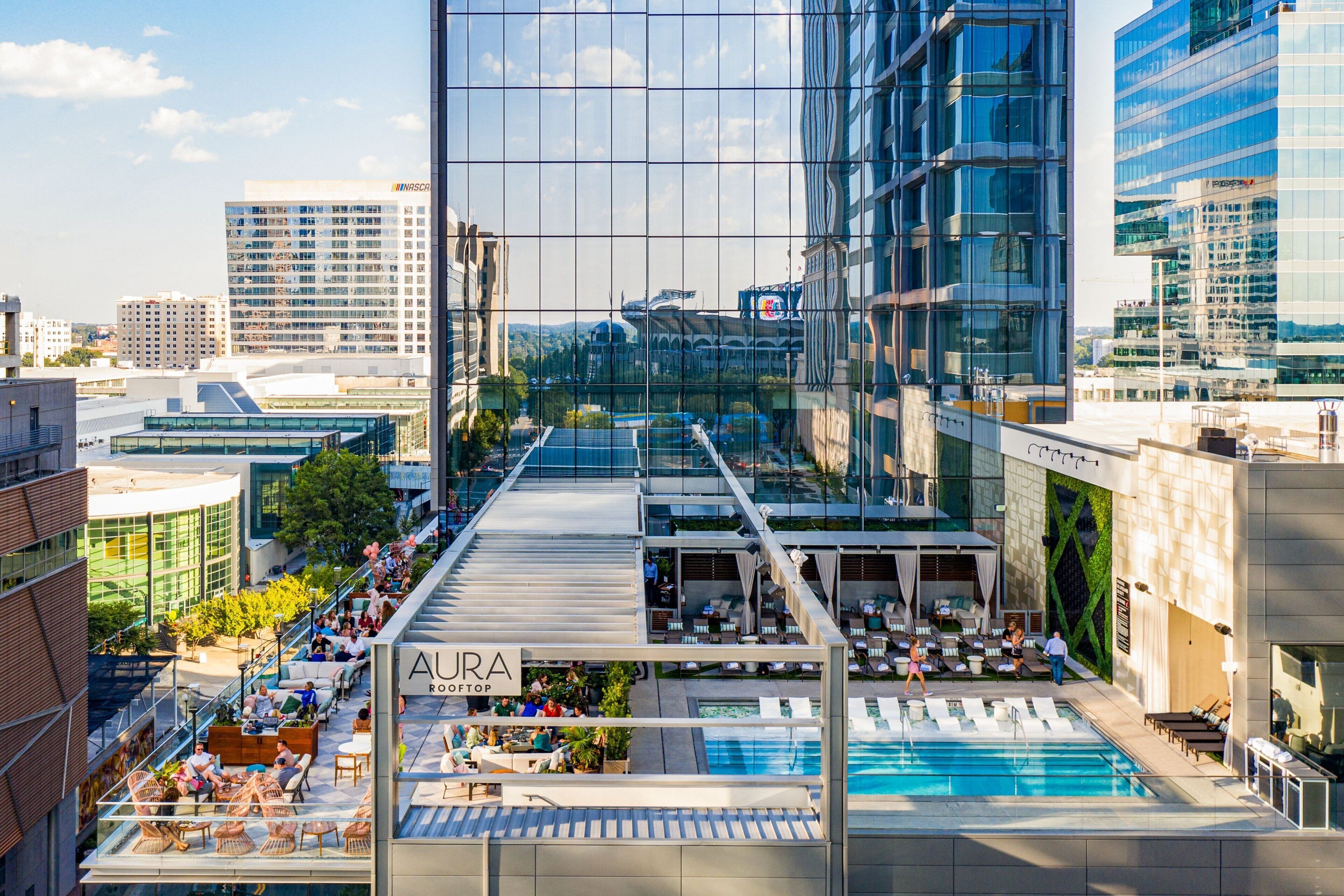 A rooftop pool area with lounge chairs and a sign for 'AURA ROOFTOP'.