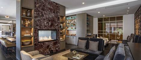 A modern living room with a fireplace, seating area, and a kitchen in the background.