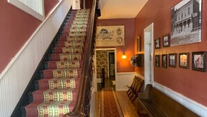 A grand staircase with patterned carpet, a wooden bench, and framed pictures on the walls. - Historic Commercial Hotel(Est. 1868)Tom Mix Suite (Osceola)