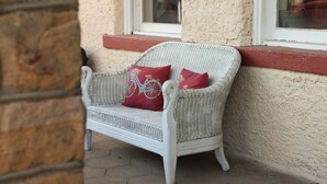 A white wicker sofa with red cushions against a textured wall, positioned near a window. - Historic Commercial Hotel(Est. 1868)Tom Mix Suite (Osceola)