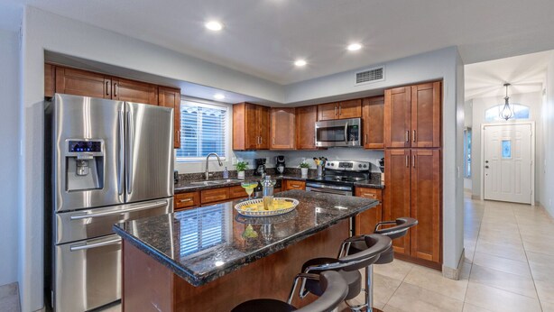 A modern kitchen with stainless steel appliances, wooden cabinets, a granite countertop, and a bar area with stools. - WOW! Hikers/Bikers/Golfers PARADISE, Pvt Htd POOL, Putt Green, Tesla Charger (Gilbert)
