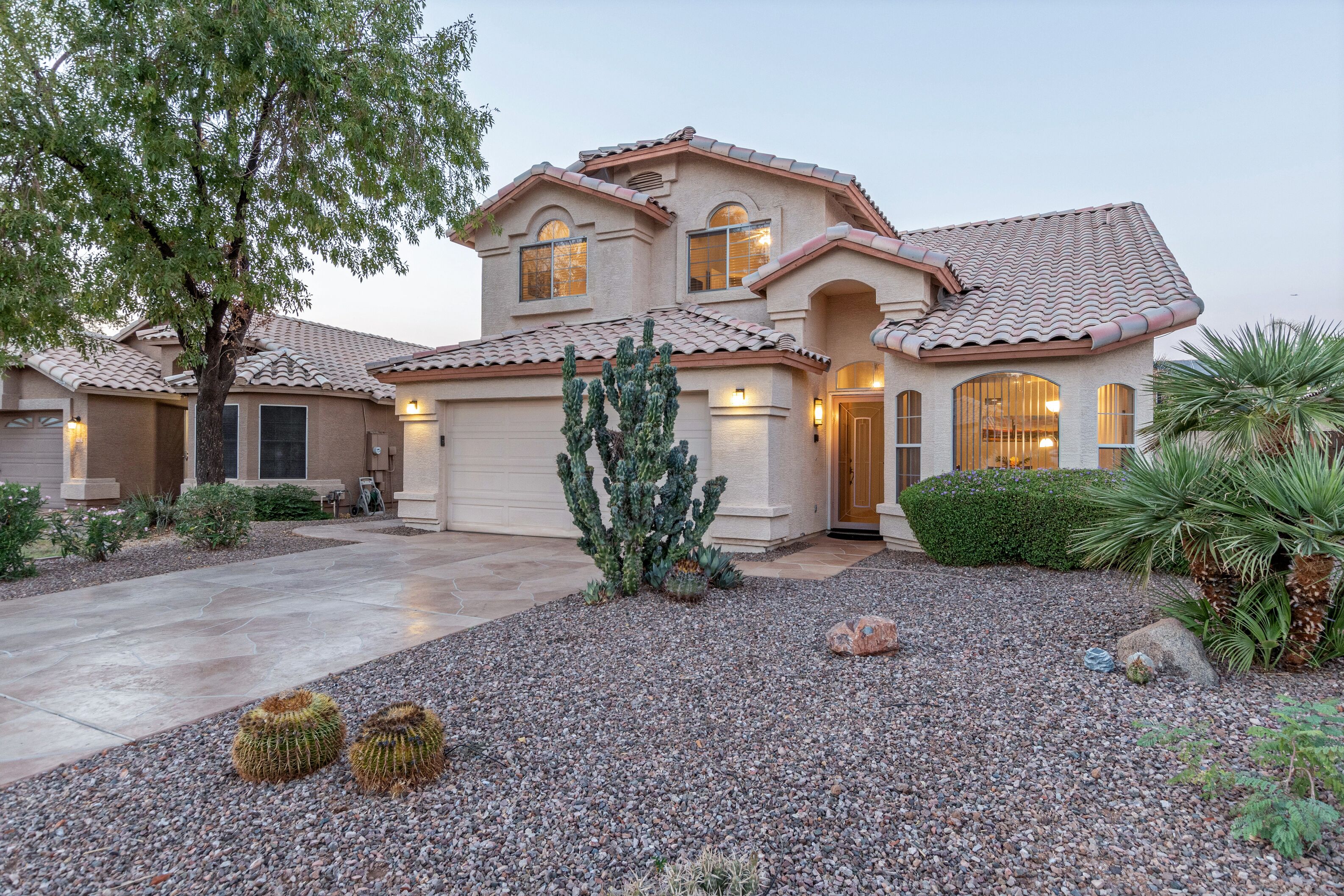 A two-story house with a tiled roof, a driveway, and a landscaped garden with cacti and shrubs.