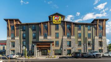 A multi-story hotel with a 'My Place' sign, featuring a stone facade, multiple windows, and a parking lot with several cars.