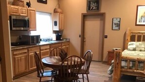 A compact kitchen with wooden cabinets, a microwave, and a dining area with a round table and chairs. - Beautiful bunkhouse in forest just hours outside Phoenix metro area (Strawberry)
