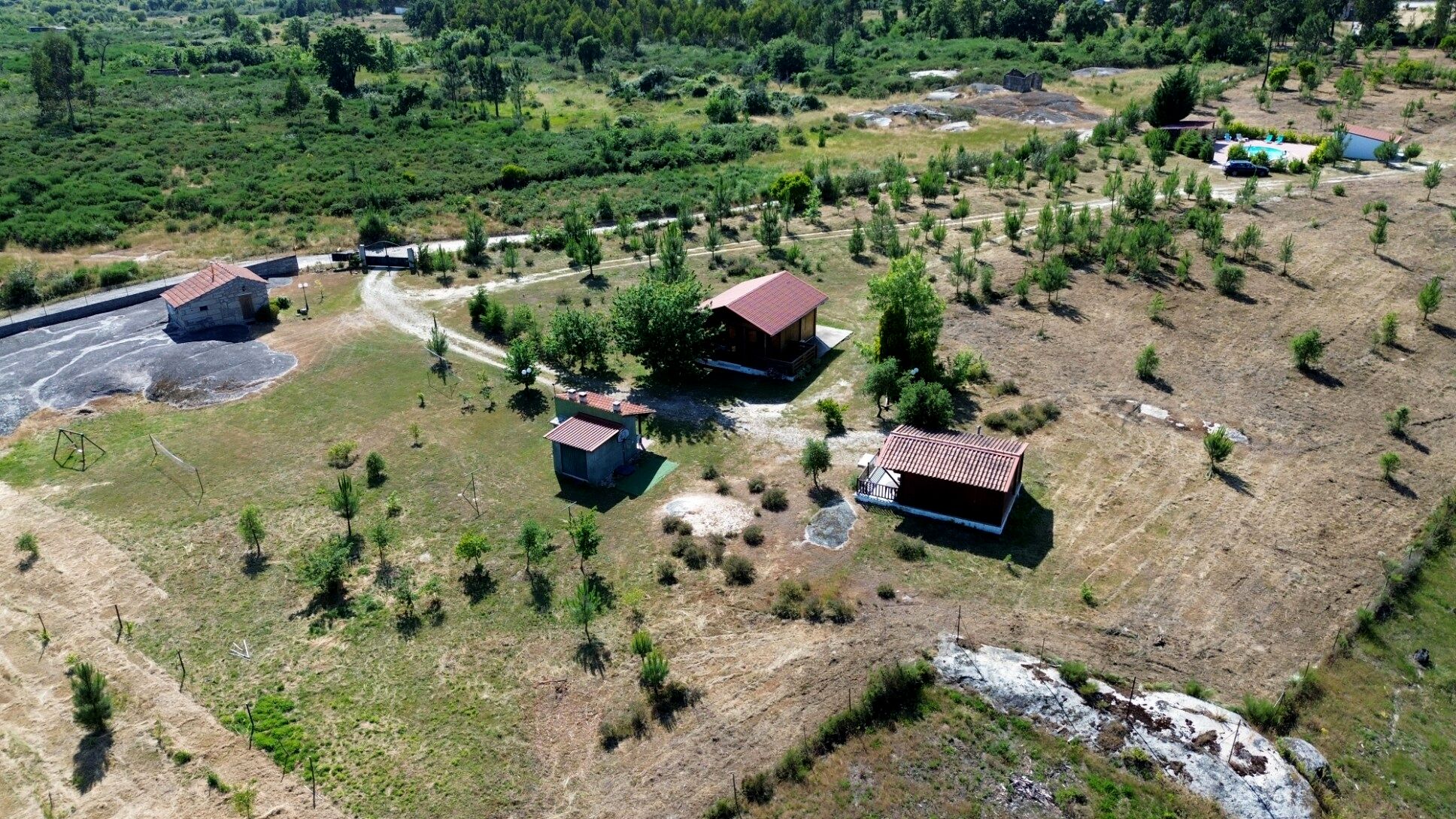 Vista aérea de una propiedad rural con varias construcciones, incluyendo una casa principal con techo rojo, edificios más pequeños y una zona de piscina.