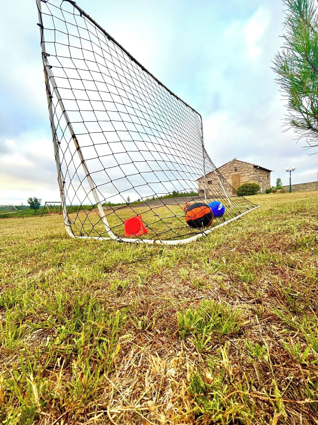 Una porta da calcio con due palloni a terra e un cono rosso nelle vicinanze.