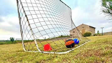 Una porta da calcio con due palloni a terra e un cono rosso nelle vicinanze.
