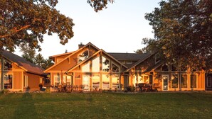 A modern house with a large glass facade, a spacious lawn, and a dining area with outdoor furniture. - 3BR Townhome | Beach Access & Pontoon Rentals (Nisswa)