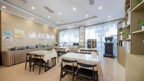 A dining area with tables and chairs, a counter with food items, and a clock on the wall. - Greentree Inn Jiaxing Tongxiang Tudian Express Hotel (Jiaxing)