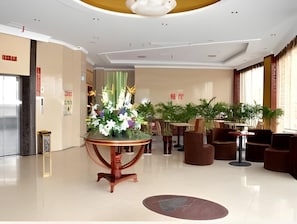 A spacious lobby with a central round table adorned with flowers, surrounded by seating areas and potted plants. - Greentree Inn Jiaxing Tongxiang Tudian Express Hotel (Jiaxing)