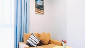 A modern living room with a beige sofa, a round yellow table with a vase of flowers, and a framed abstract artwork on the wall. - Greentree Inn Jiaxing Tongxiang Tudian Express Hotel (Jiaxing)