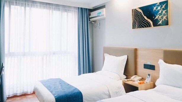 A hotel room with two beds, a large window with sheer curtains, a wall-mounted air conditioner, and a piece of abstract art. - Greentree Inn Jiaxing Tongxiang Tudian Express Hotel (Jiaxing)