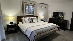A bedroom with a bed, two bedside tables with lamps, a dresser, a television, and an air conditioning unit. - Newly updated, great for multiple families up to 12 & pets; read reviews! (Clifton Township)
