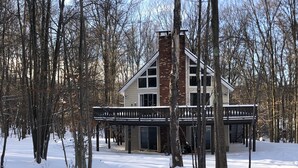 A two-story house with a brick chimney, surrounded by snow-covered ground and bare trees. - Newly updated, great for multiple families up to 12 & pets; read reviews! (Clifton Township)