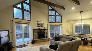 A spacious living room with a stone fireplace, large windows, a television, and a dining area. - Newly updated, great for multiple families up to 12 & pets; read reviews! (Clifton Township)