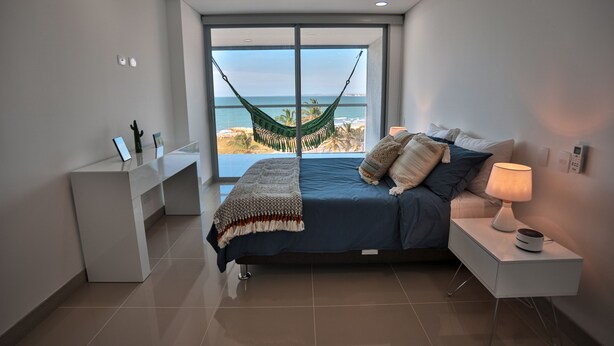 Un dormitorio con cama, mesita de noche, escritorio y vista al océano.