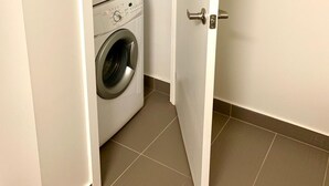 Una sala de lavandería con dos lavadoras apiladas, una puerta y suelo de baldosas.