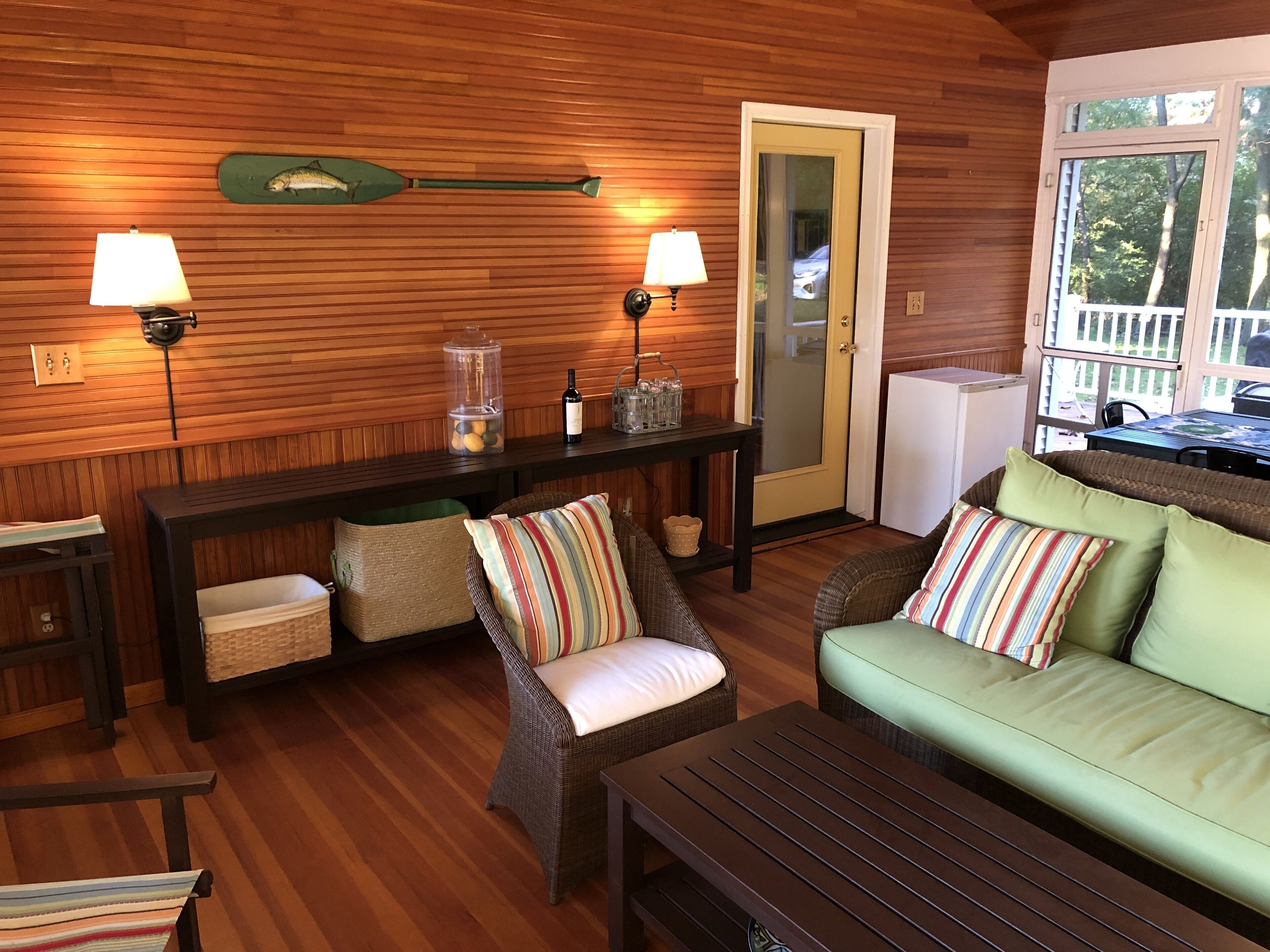 Une pièce chaleureuse avec un plancher en bois, un canapé vert, un fauteuil à rayures, une table en bois foncé et deux lampes.