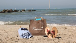 Une scène de plage avec un sac marron, une serviette enroulée et une paire de sandales sur le sable.