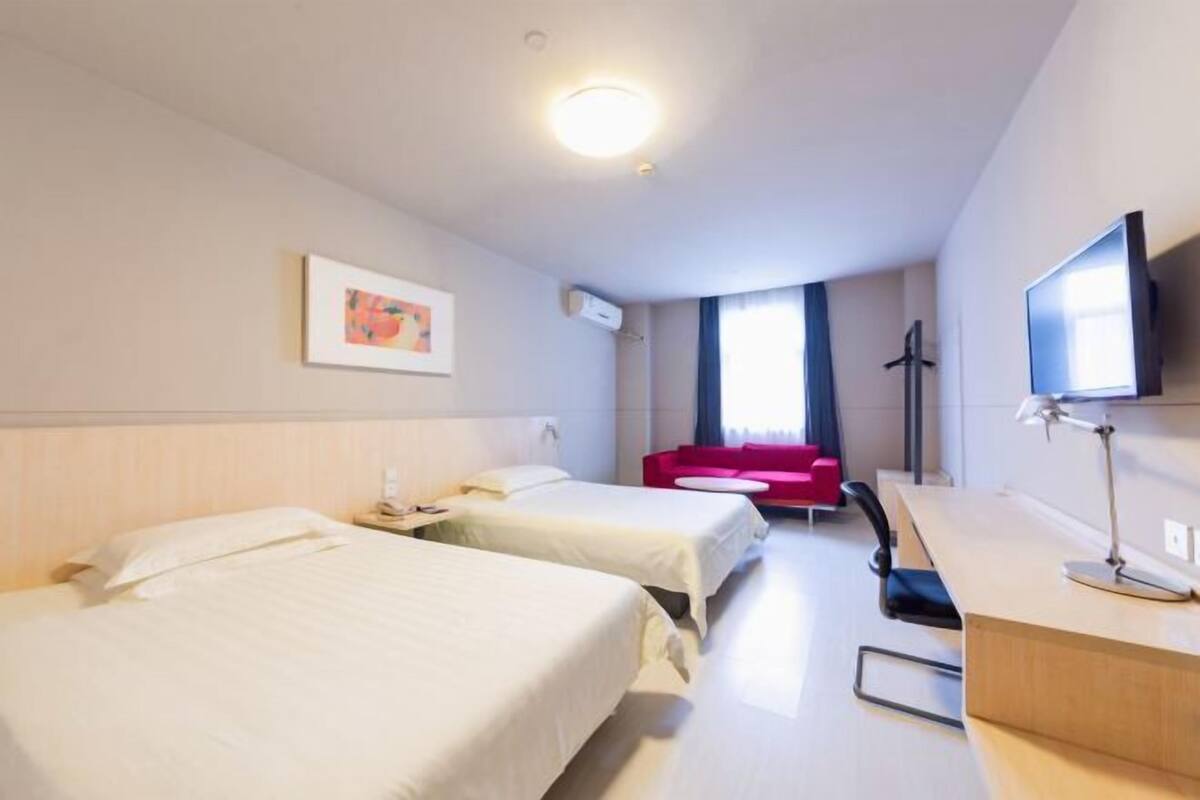 Hotellihuone, jossa on kaksi sänkyä, työpöytä, televisio, punainen sohva ja taulu seinällä.