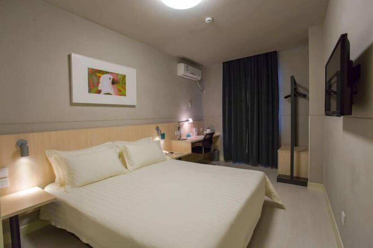 Hotellihuone, jossa on sänky, yöpöytä, työpöytä, tuoli ja televisio.