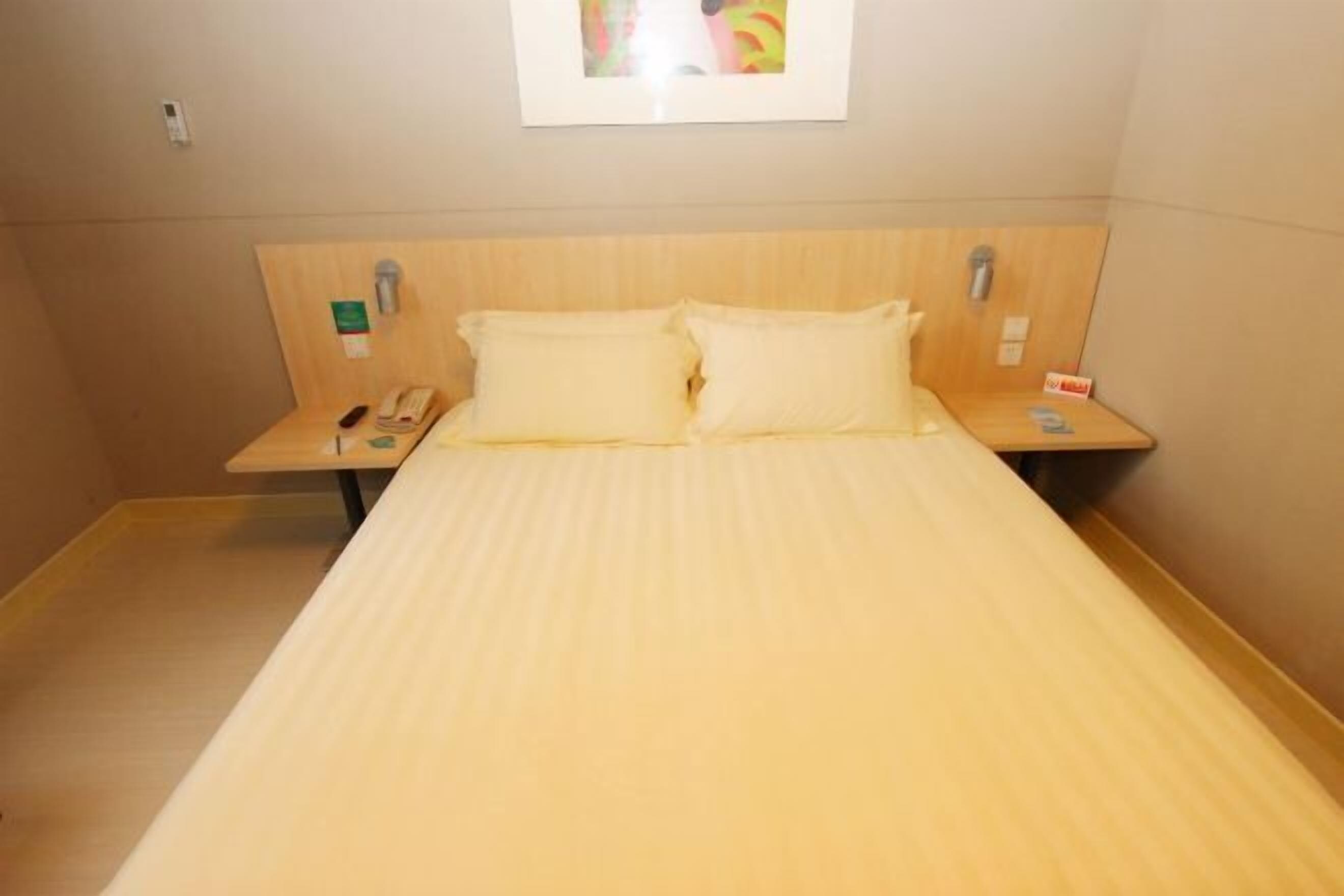 Quarto de hotel com cabeceira de madeira, duas almofadas, mesa de cabeceira com telefone e quadro na parede.