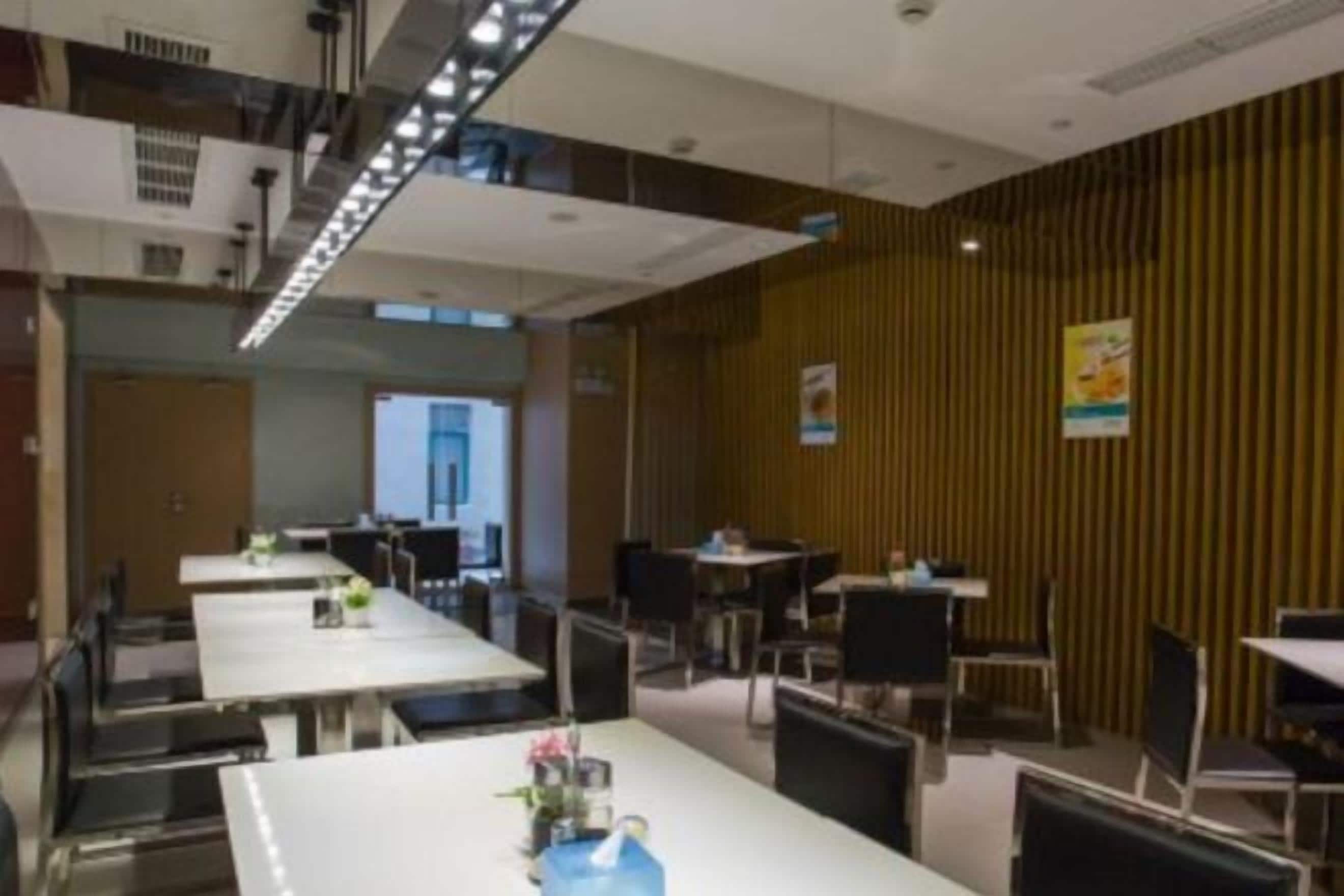 A modern dining area with multiple tables and chairs, a staircase, and a wooden accent wall.