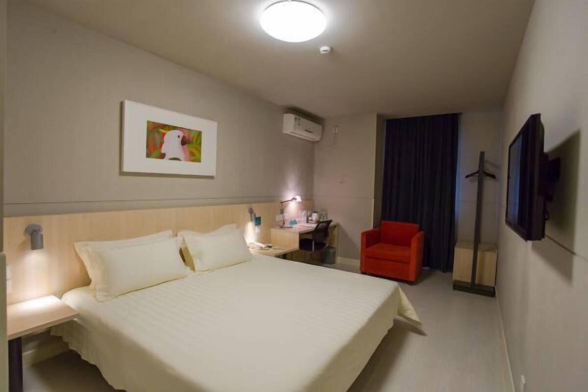 Hotellihuone, jossa on sänky, työpöytä, tuoli, ilmastointilaite, taulu ja peili.